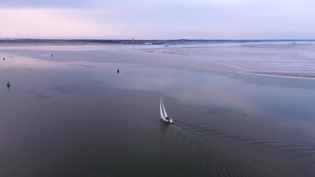 Aerial drone footage of a sailboat sailing across Wadden sea towards the Frisian island of Terschelling, glass water, calm, sea with tidal sandbanks 