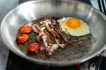 Scrambled eggs with bacon and cherry tomatoes in a pan. Concept: delicious breakfast.
