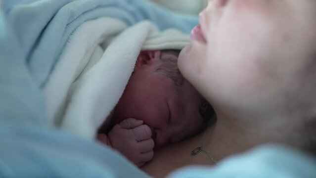 Newborn baby resting on mother's chest right after birth emphasizing skin to skin contact, real life authentic infant covered by blankets to keep warm in postpartum