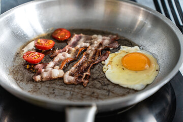 Scrambled eggs with bacon and cherry tomatoes in a pan. Concept: delicious breakfast.