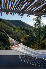 A hammock is hanging from a tropical hut in front of a mountain in summertime