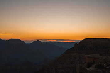 Scenic sunset over vast canyon with warm gradient colors from orange to blue. Silhouettes of rock formations visible against twilight sky. Possibly Grand Canyon viewpoint. Breathtaking natural beauty.
