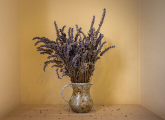 Dried lavender in a jug. With yellow wall and tiled shelf. Landscape orientation.