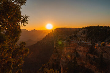 Scenic sunset at Grand Canyon with red rock layers glowing in golden light, vast horizon, and...
