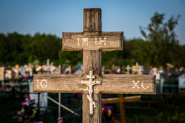 Wooden cross in cemetery with XC symbol under sky, grass, religious item