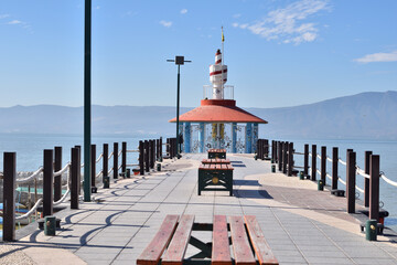A pier in Chapala Lake with a lighthouse and benches. The pier is empty and the water is calm. The lighthouse is tall and white