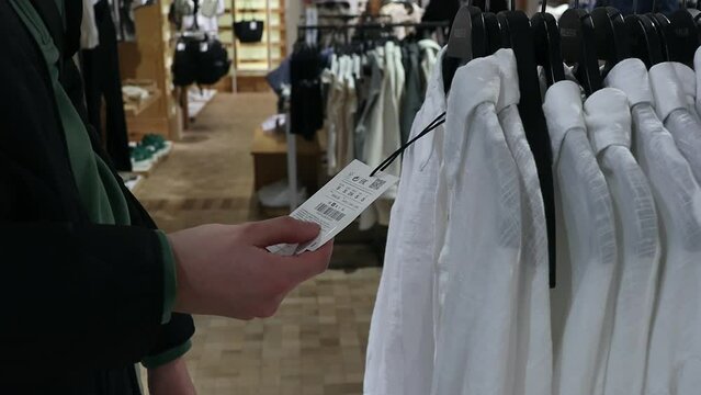 A girl studies the price tag and label of a white shirt in a store.