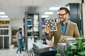A smiling man holding a ceramic tile, searching for some interesting designs.
