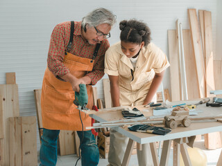 Teenaged girls learn to use an electronic saw and play with their grandfather in the wooden...