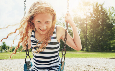 Girl, portrait and smile with park, swing and nature for outdoor fun and play with fresh air. Child, tree and playground with summer, freedom and school holiday or break outside with happiness