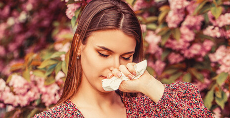 Woman wiping her nose.Woman sneezing into a handkerchief near a tree full of blossoms. She is...