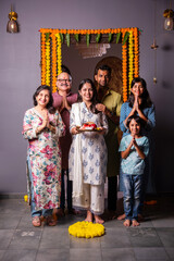 Indian happy family with puja thali in welcoming pose at entrance door