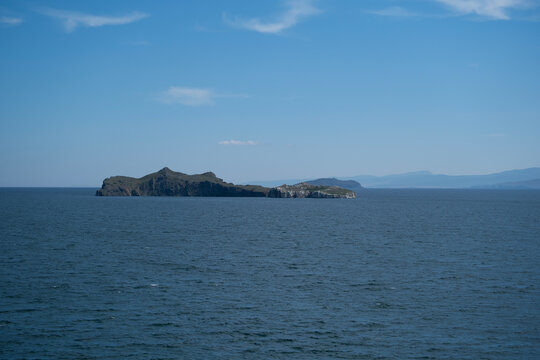 Water landscape,distant view of rocky uninhabited Lake Baikal island,on horizon faintly visible mountains of opposite shore, summer sunny day. Beautiful wild nature travel concept. Deep waves surface.