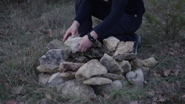 slow motion young caucasian man in the forest finishing a firepit of stones to light a fire inside
