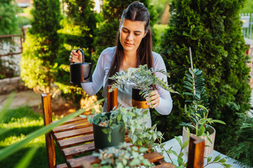 One young caucasian woman is taking care of her plants using plant mister and water can	