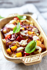 Penne pasta baked with peppers, red onion and mozzarella. Bright wooden background.	