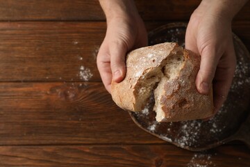 Man breaking loaf of fresh bread at wooden table, top view. Space for text
