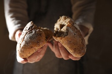 Man breaking loaf of fresh bread on dark background, closeup
