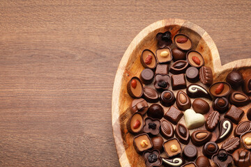 Heart shaped plate with delicious chocolate candies on wooden table, top view. Space for text