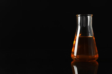 Glass flask with yellow oil on black background, space for text