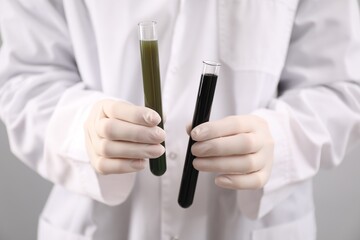 Woman holding test tubes with different types of crude oil on light background, closeup