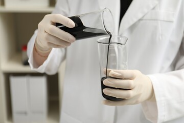 Laboratory worker pouring black crude oil into flask indoors, closeup
