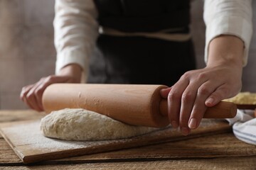 Woman rolling raw dough at wooden table, closeup