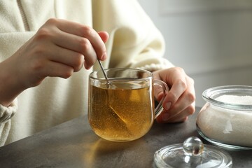 Woman stirring sugar in tea at grey table, closeup