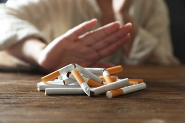 Stop smoking. Woman making stop gesture at wooden table, focus on whole and broken cigarettes