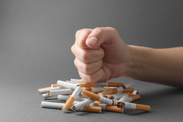 Stop smoking. Woman crushing cigarettes on grey background, closeup