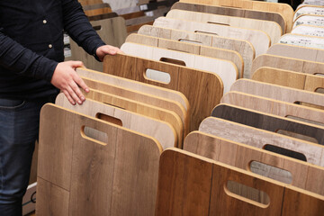 Man choosing wooden flooring among different samples in shop, closeup
