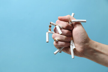 Stop smoking. Man holding broken cigarettes on light blue background, closeup. Space for text