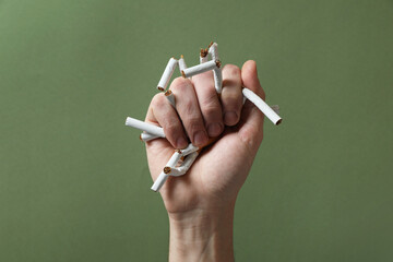 Stop smoking. Man holding broken cigarettes on olive background, closeup