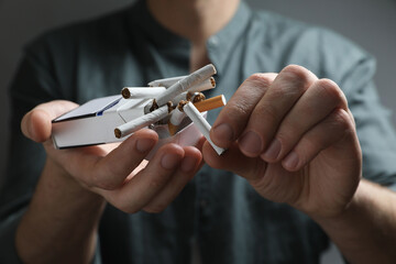Stop smoking. Man holding pack with broken cigarettes on grey background, closeup