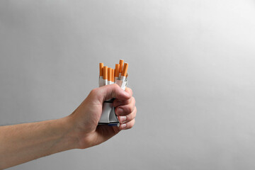Stop smoking. Man holding pack with cigarettes on grey background, closeup. Space for text
