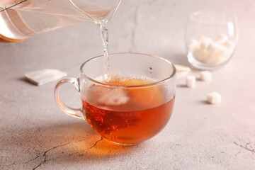 Pouring hot water into cup with tea bag on light grey textured table, closeup