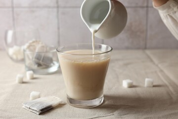 Pouring milk into cup with tea on light table, closeup