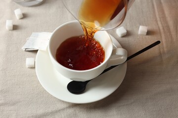 Pouring warm tea into cup on light table, closeup