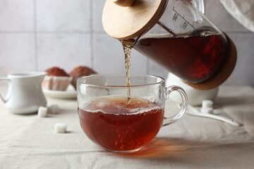 Pouring warm tea into cup on light table, closeup