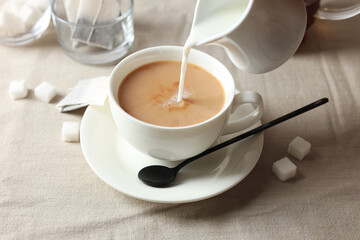Pouring milk into cup with tea on light table, closeup