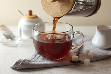 Pouring warm tea into cup on white wooden table, closeup