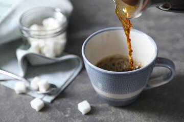 Pouring hot coffee into cup on grey table, closeup