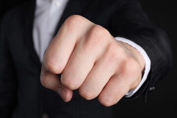 Businessman showing fist with space for tattoo on black background, closeup