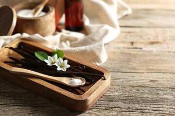 Vanilla pods, flowers, leaves and spoon with sugar on wooden table, closeup. Space for text