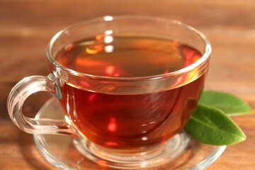 Aromatic tea in glass cup and green leaves on wooden table, closeup
