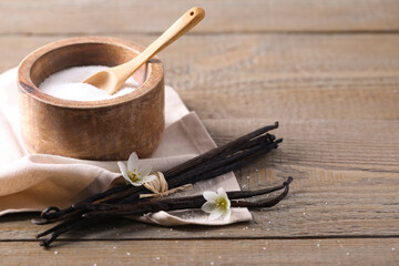 Vanilla pods, sugar in bowl and flowers on wooden table, closeup