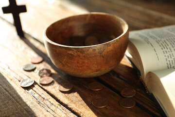 Donate and give concept. Bowl with coins, cross and Bible on wooden table in sunlights, selective focus