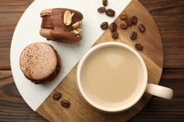 Cup of coffee and delicious macarons on wooden table, top view