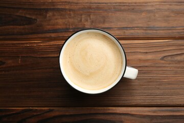 Tasty cappuccino in cup on wooden table, top view