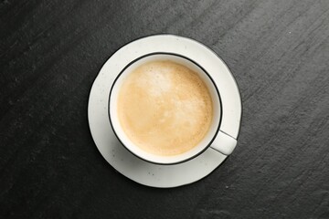 Tasty cappuccino in cup and saucer on dark textured table, top view
